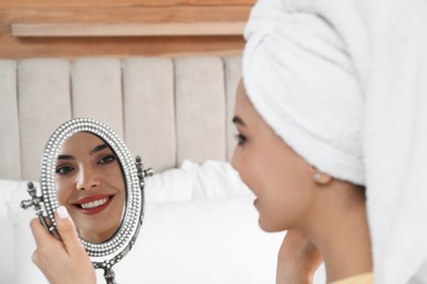 Beautiful woman with mirror applying makeup in bedroom, closeup