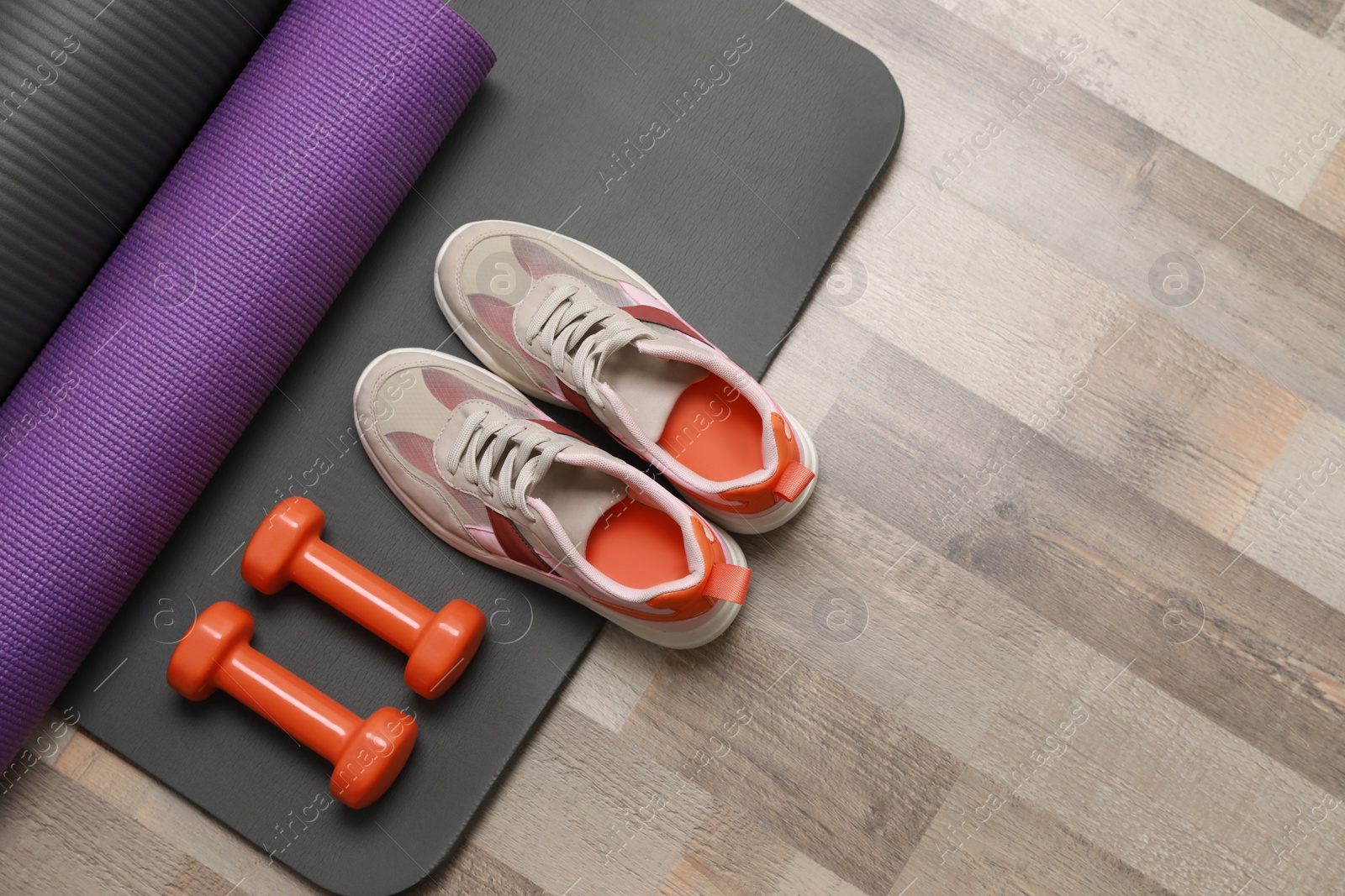 Photo of Dumbbells, sneakers and mats on wooden floor, flat lay. Space for text