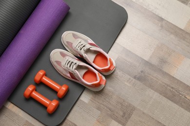 Photo of Dumbbells, sneakers and mats on wooden floor, flat lay. Space for text