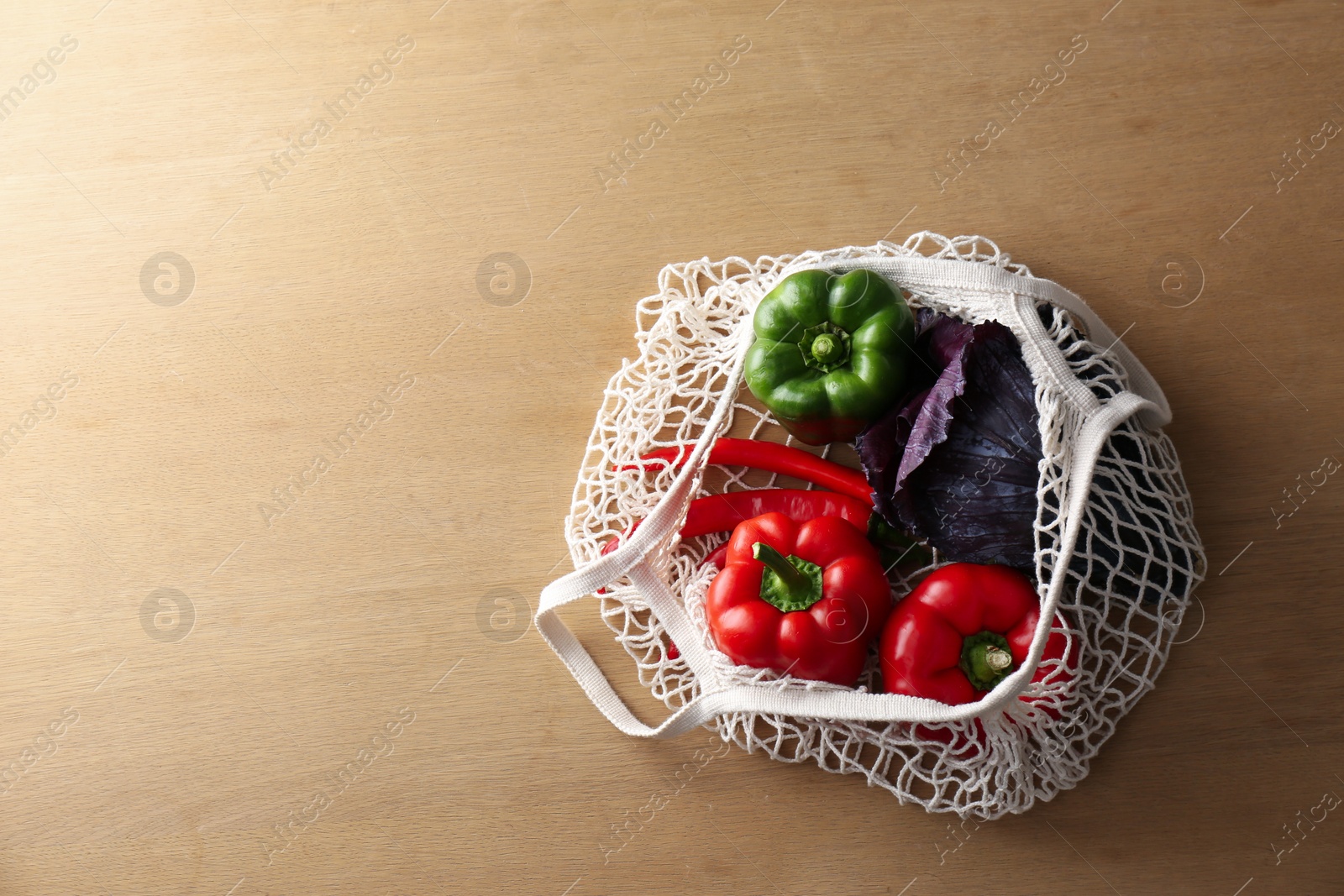 Photo of Different fresh vegetables in eco mesh bag on wooden table, top view