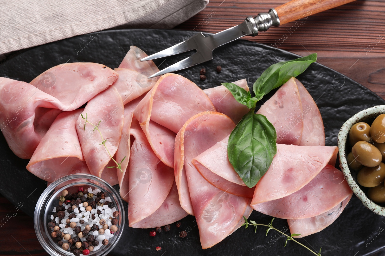 Photo of Tasty ham with basil, olives, sea salt, peppercorns and carving fork on wooden table, top view