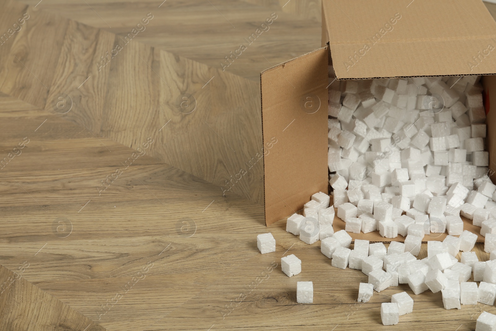 Photo of Overturned cardboard box with styrofoam cubes on wooden floor. Space for text