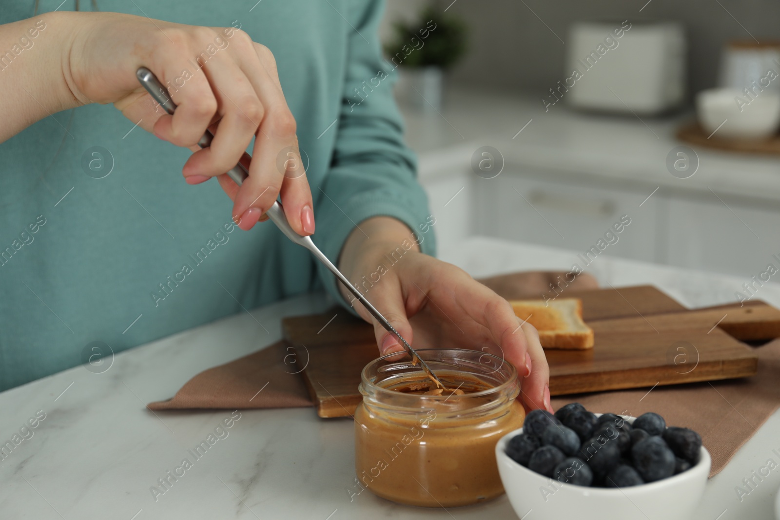Photo of Woman taking tasty nut butter onto knife at marble table, closeup