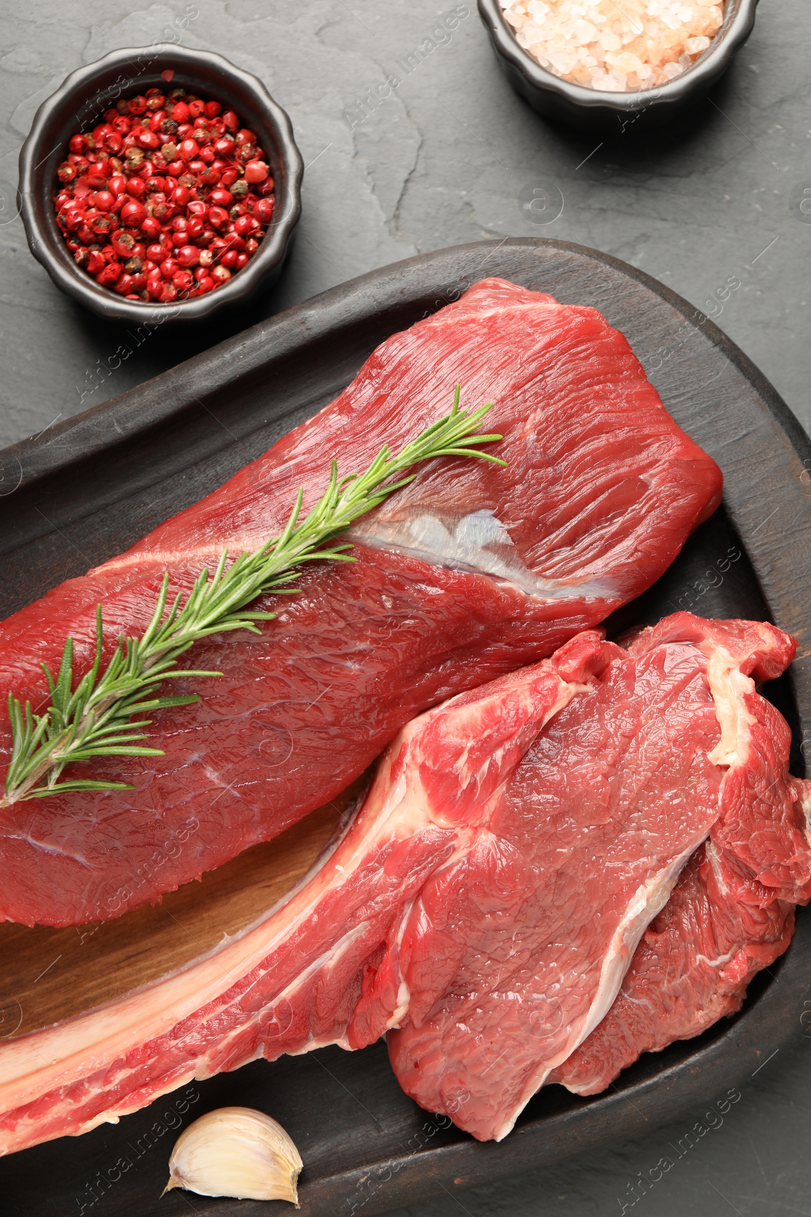 Photo of Pieces of raw beef meat and spices on grey table, flat lay