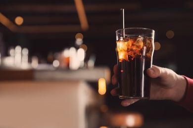 Man holding glass of refreshing cola indoors, closeup. Space for text