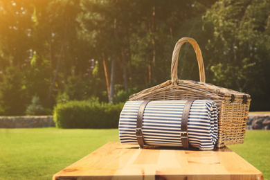 Image of Picnic basket with blanket on wooden table in green park 