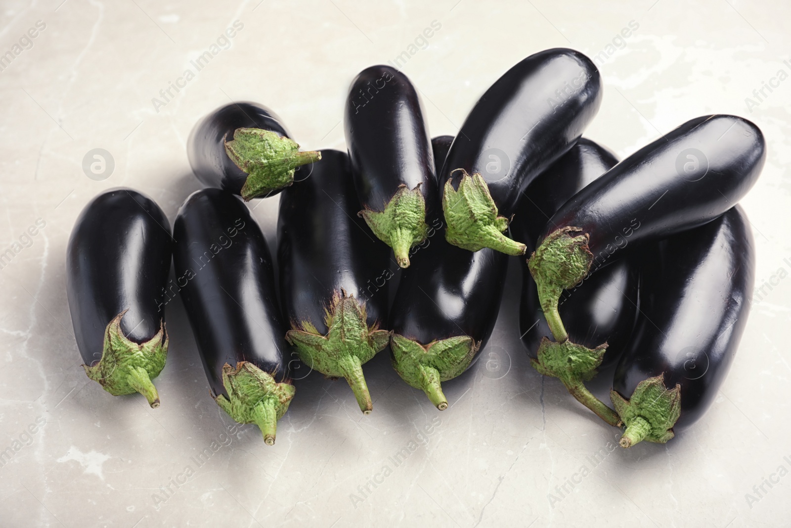 Photo of Pile of raw ripe eggplants on light background