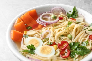 Photo of Bowl of tasty noodles with egg and vegetables on table, closeup