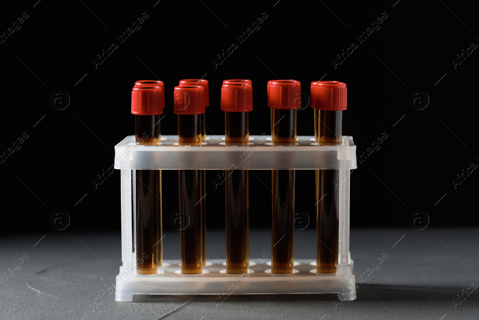 Photo of Test tubes with brown liquid in stand on grey table