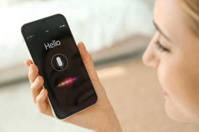 Young woman using voice search on smartphone indoors, closeup