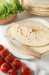 Tasty homemade tortillas, tomatoes, lettuce and knife on white wooden table