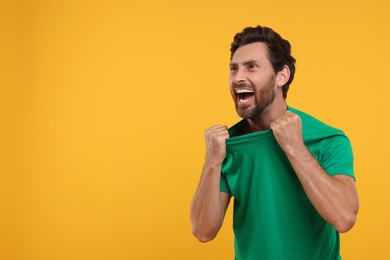 Emotional sports fan celebrating on orange background, space for text