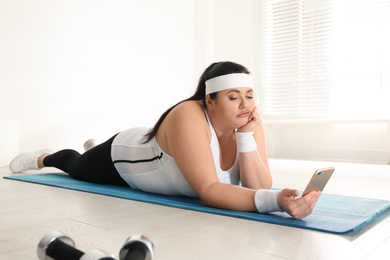 Photo of Lazy overweight woman using mobile phone instead of training at gym