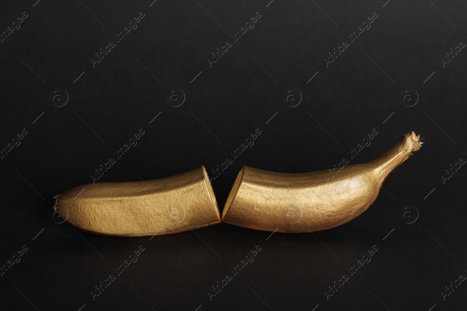 Photo of Gold painted cut banana on black background