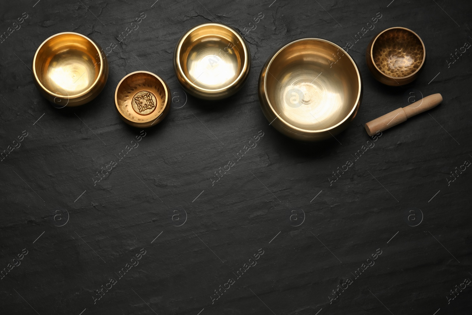 Photo of Golden singing bowls and mallet on black table, flat lay. Space for text