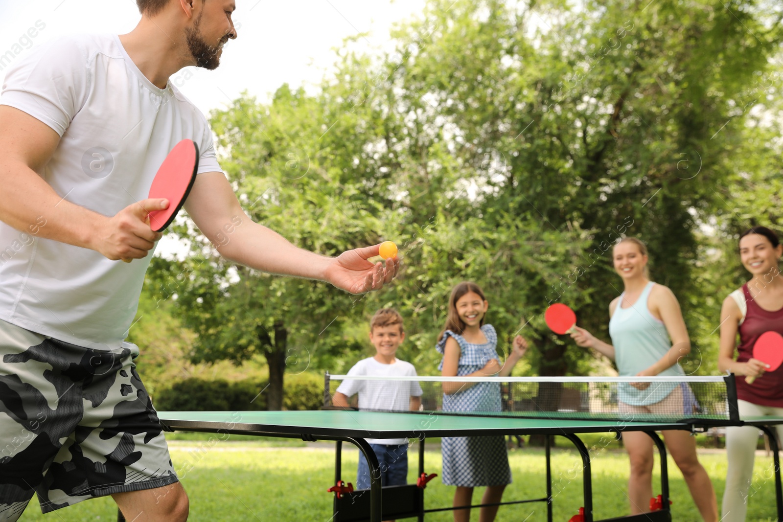 Photo of Happy family with children playing ping pong in park