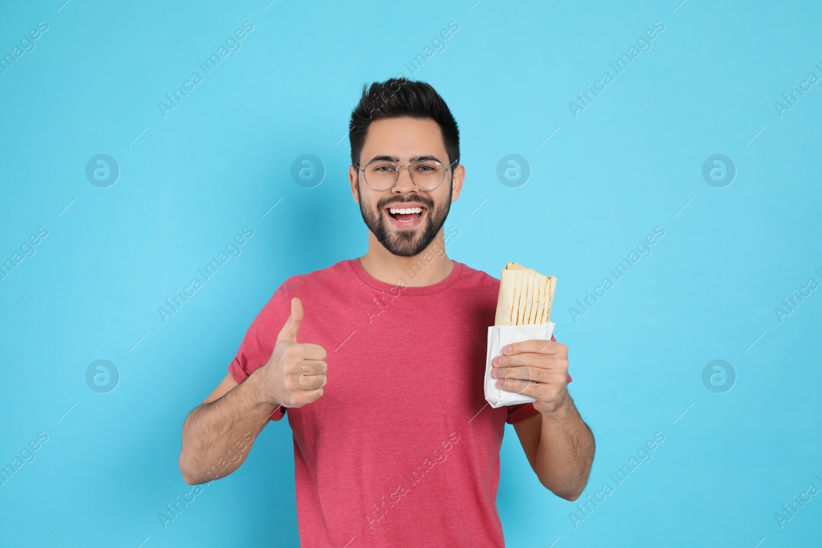 Photo of Happy young man with tasty shawarma showing thumb up on turquoise background