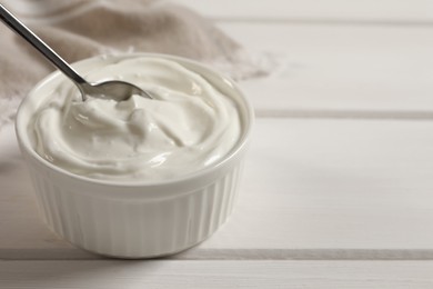 Photo of Taking yogurt with spoon from bowl at white wooden table, space for text