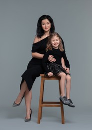 Beautiful mother with little daughter on stool against grey background