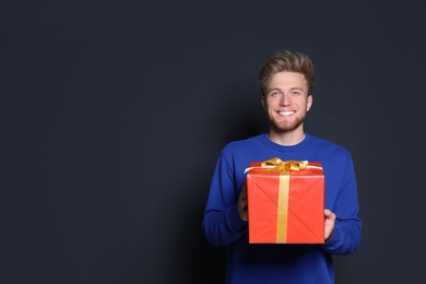 Photo of Young man with Christmas gift on dark background. Space for text
