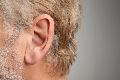 Photo of Closeup view of man against light grey background, focus on ear