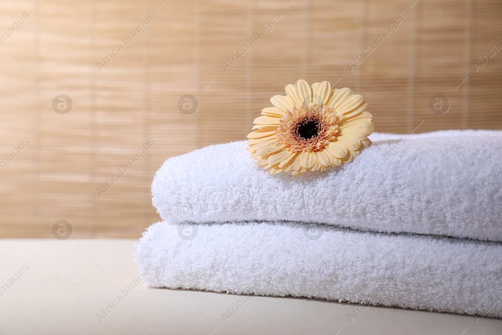 Photo of Stacked terry towels and flower on white table indoors, space for text