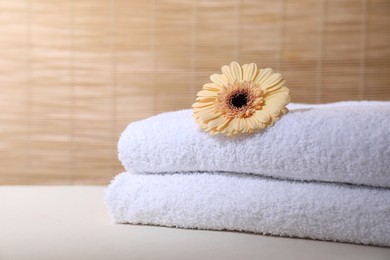 Photo of Stacked terry towels and flower on white table indoors, space for text