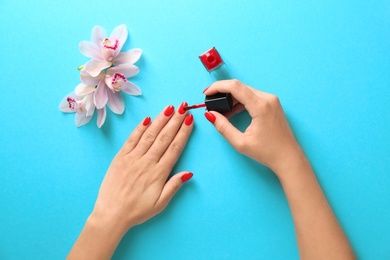 Woman applying bright nail polish on color background, top view