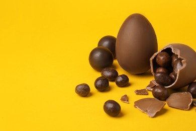 Tasty whole and broken chocolate eggs with candies on orange background. Space for text