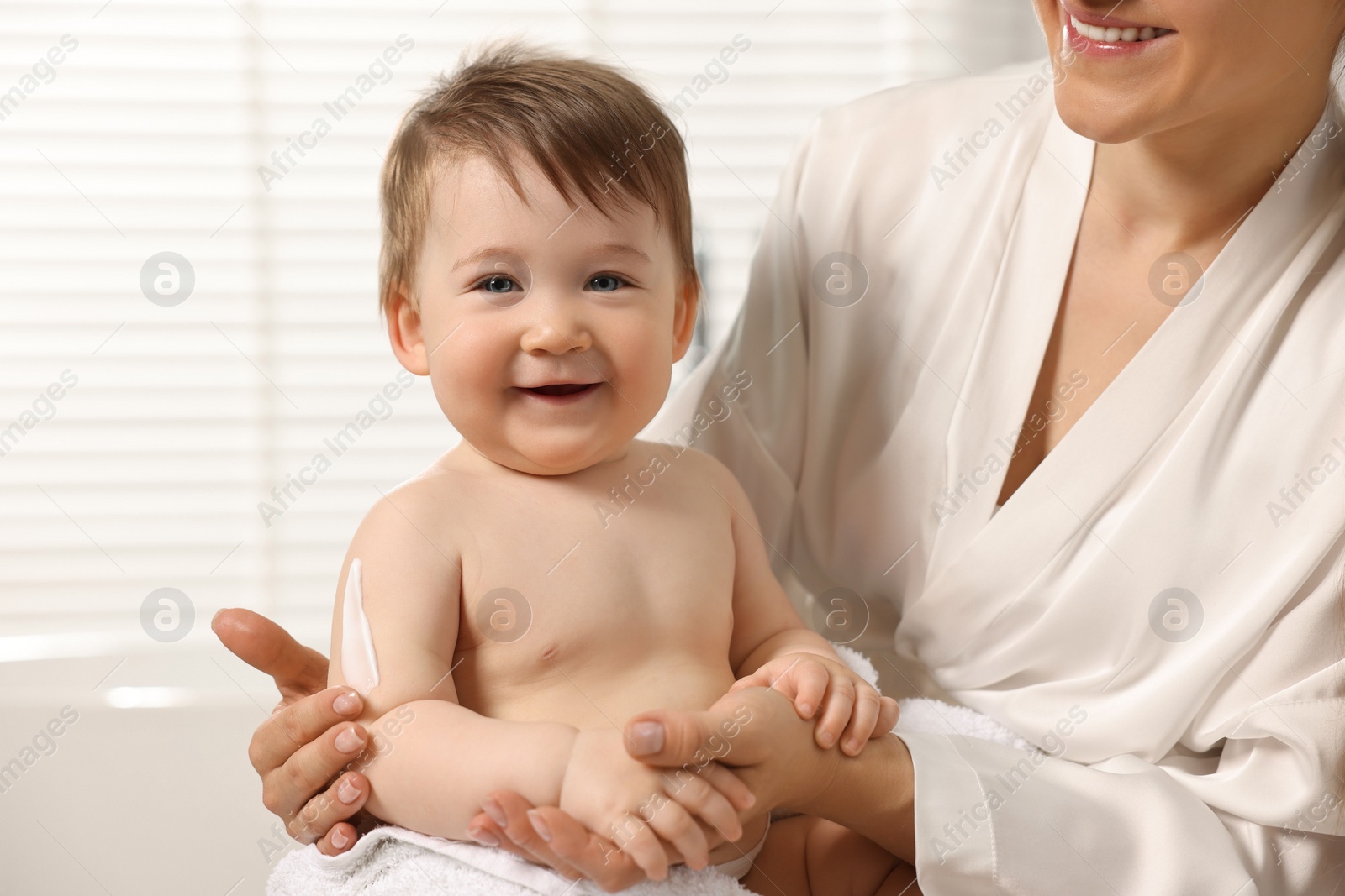 Photo of Mother applying body cream onto baby`s skin indoors, closeup