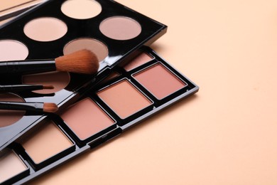 Colorful contouring palettes and brushes on beige background, closeup. Professional cosmetic product