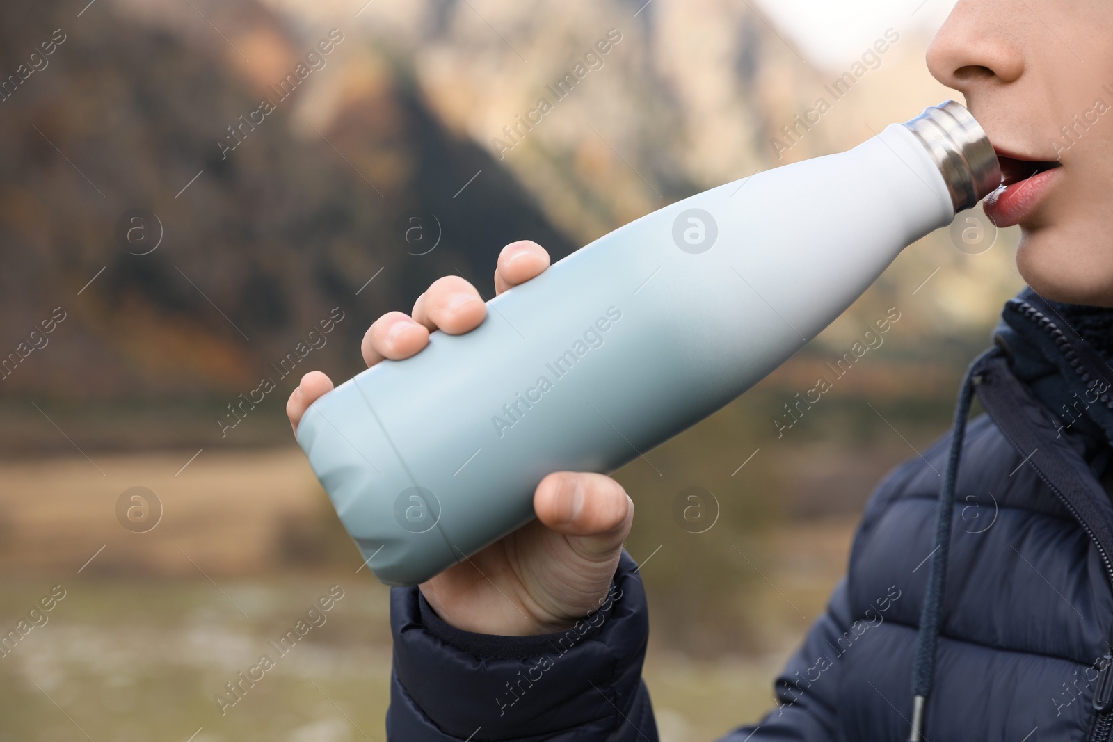 Photo of Boy drinking hot beverage from thermo bottle in mountains, closeup