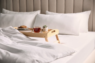 Photo of Wooden tray with breakfast and book near soft blanket on bed