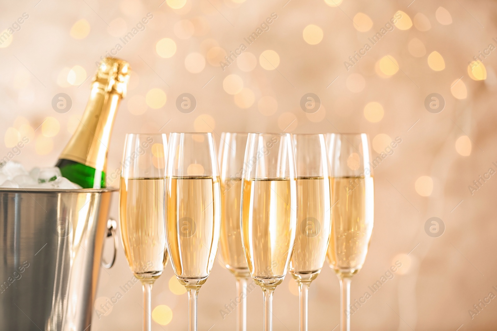 Photo of Glasses with champagne and bottle in bucket against blurred lights