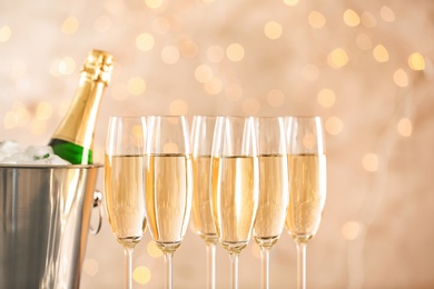 Photo of Glasses with champagne and bottle in bucket against blurred lights