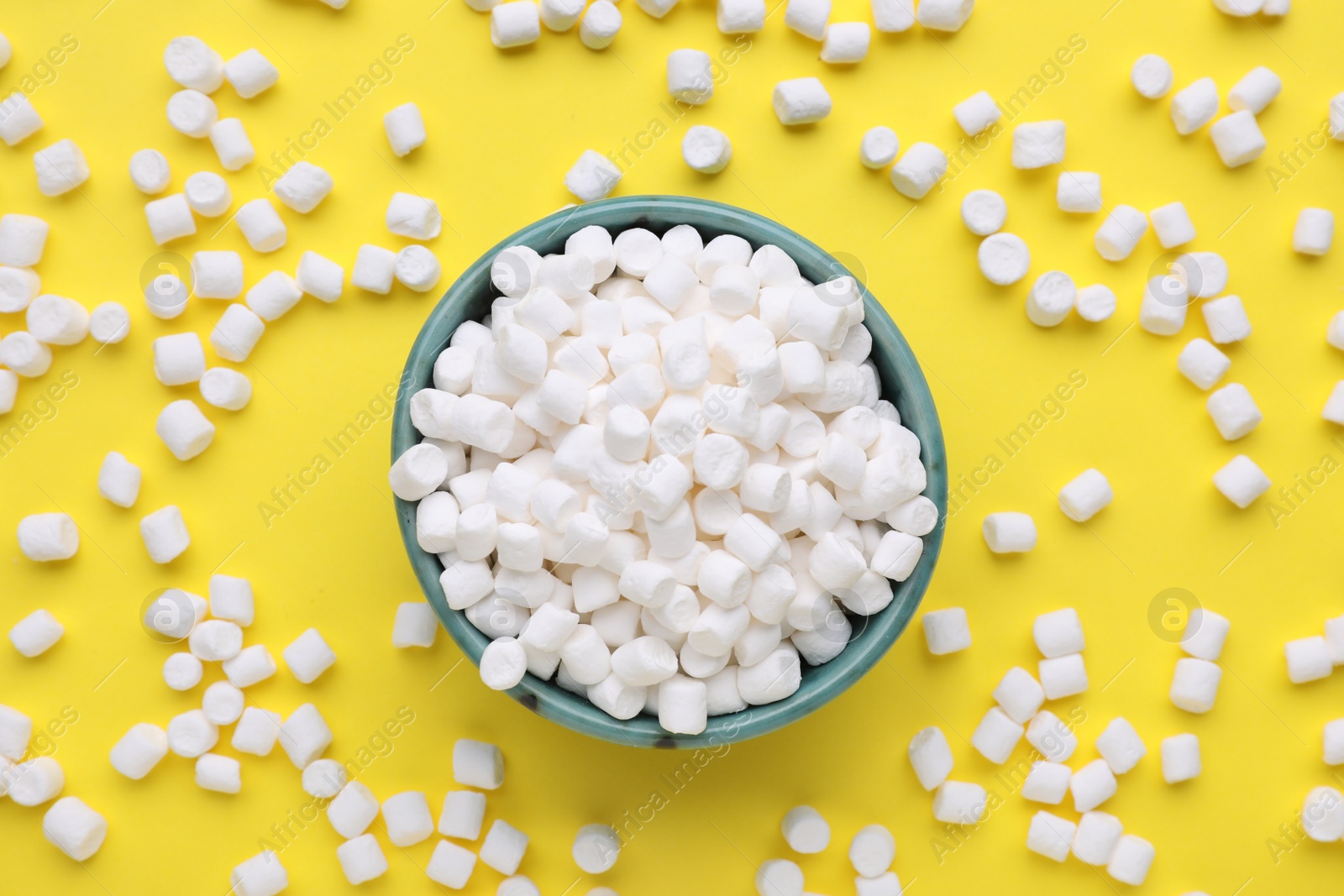 Photo of Bowl with delicious marshmallows on yellow background, flat lay