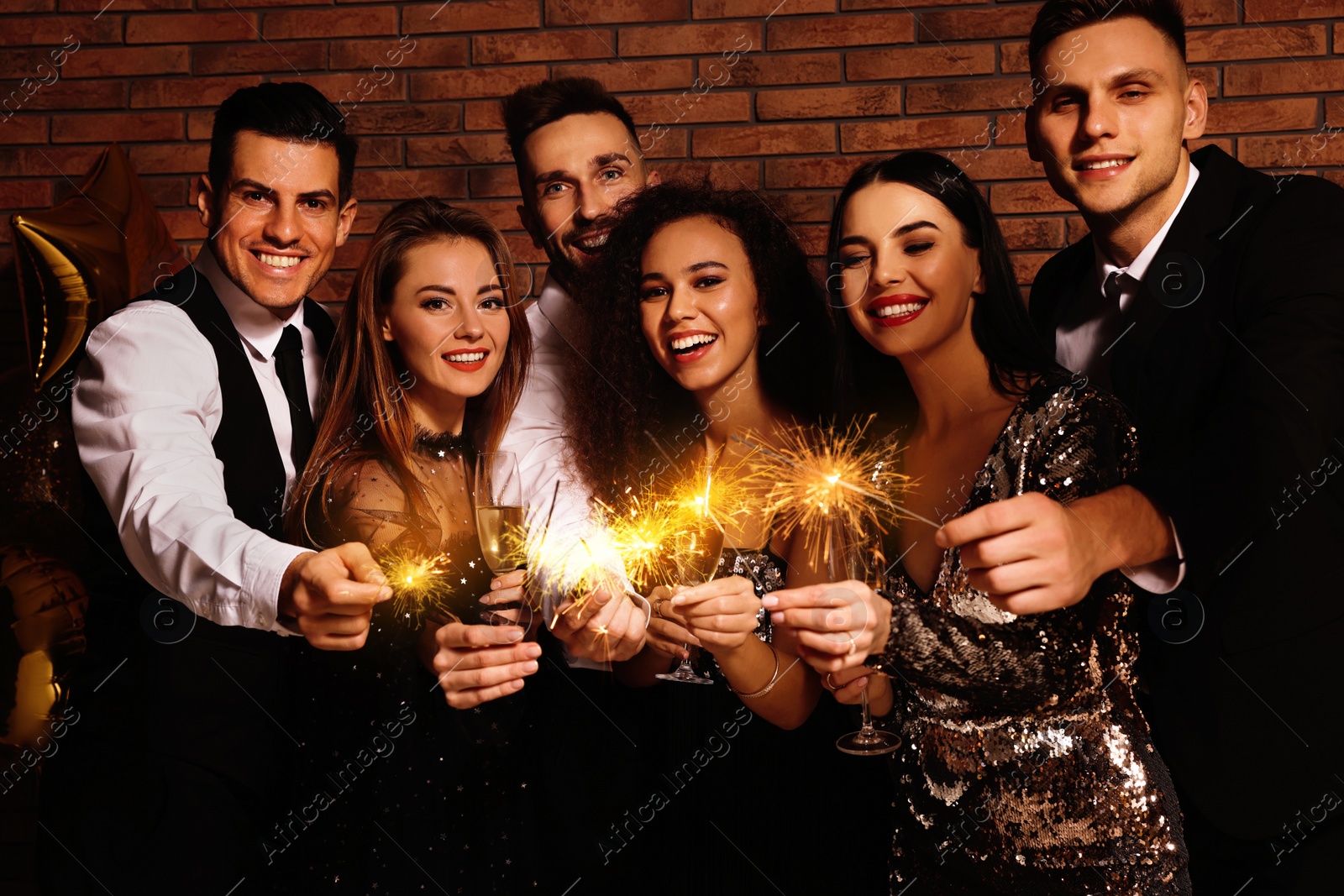 Photo of Happy friends with glasses of sparkling wine and sparklers celebrating New Year indoors