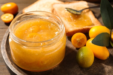 Photo of Delicious kumquat jam and fresh fruits on wooden tray