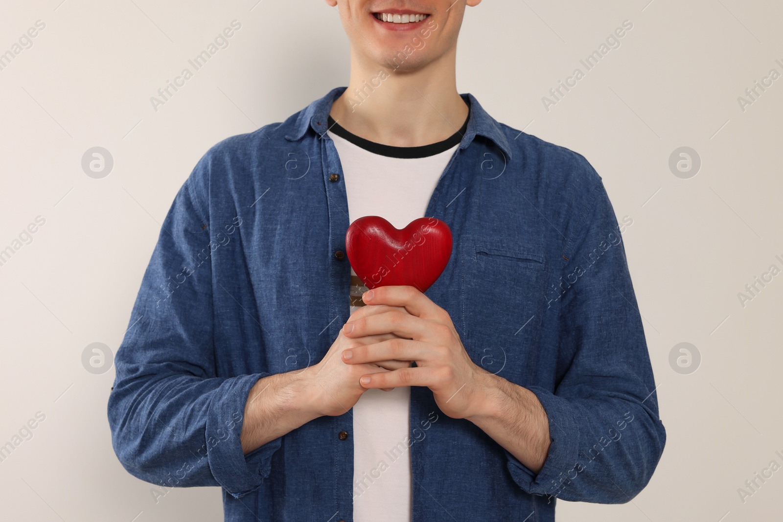 Photo of Happy volunteer holding red heart with hands on light background, closeup