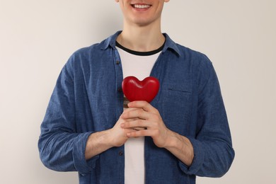 Photo of Happy volunteer holding red heart with hands on light background, closeup
