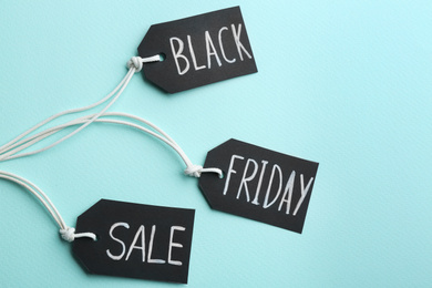 Photo of Tags with words BLACK FRIDAY SALE on turquoise background, flat lay