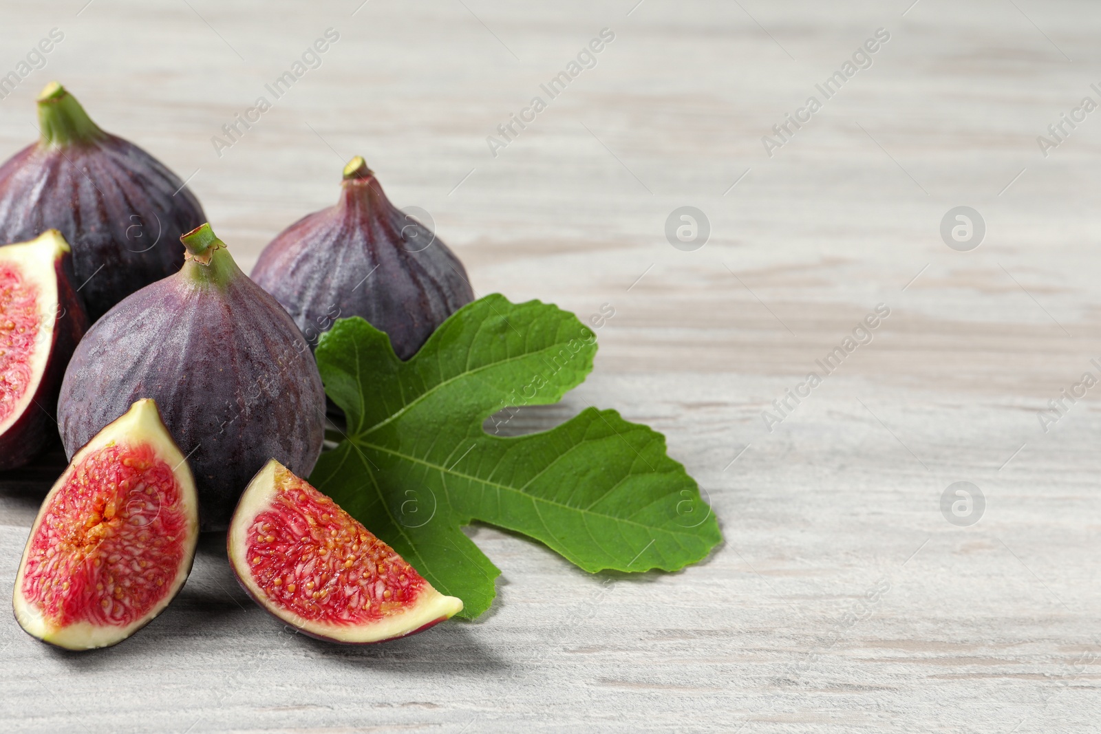 Photo of Whole and cut ripe figs with leaf on light wooden table, closeup. Space for text