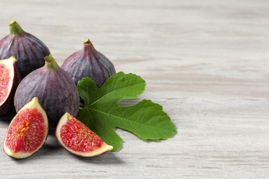 Photo of Whole and cut ripe figs with leaf on light wooden table, closeup. Space for text