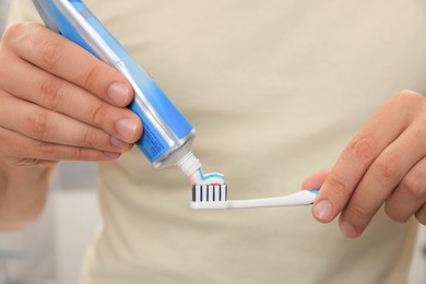 Photo of Man applying toothpaste on brush against blurred background, closeup