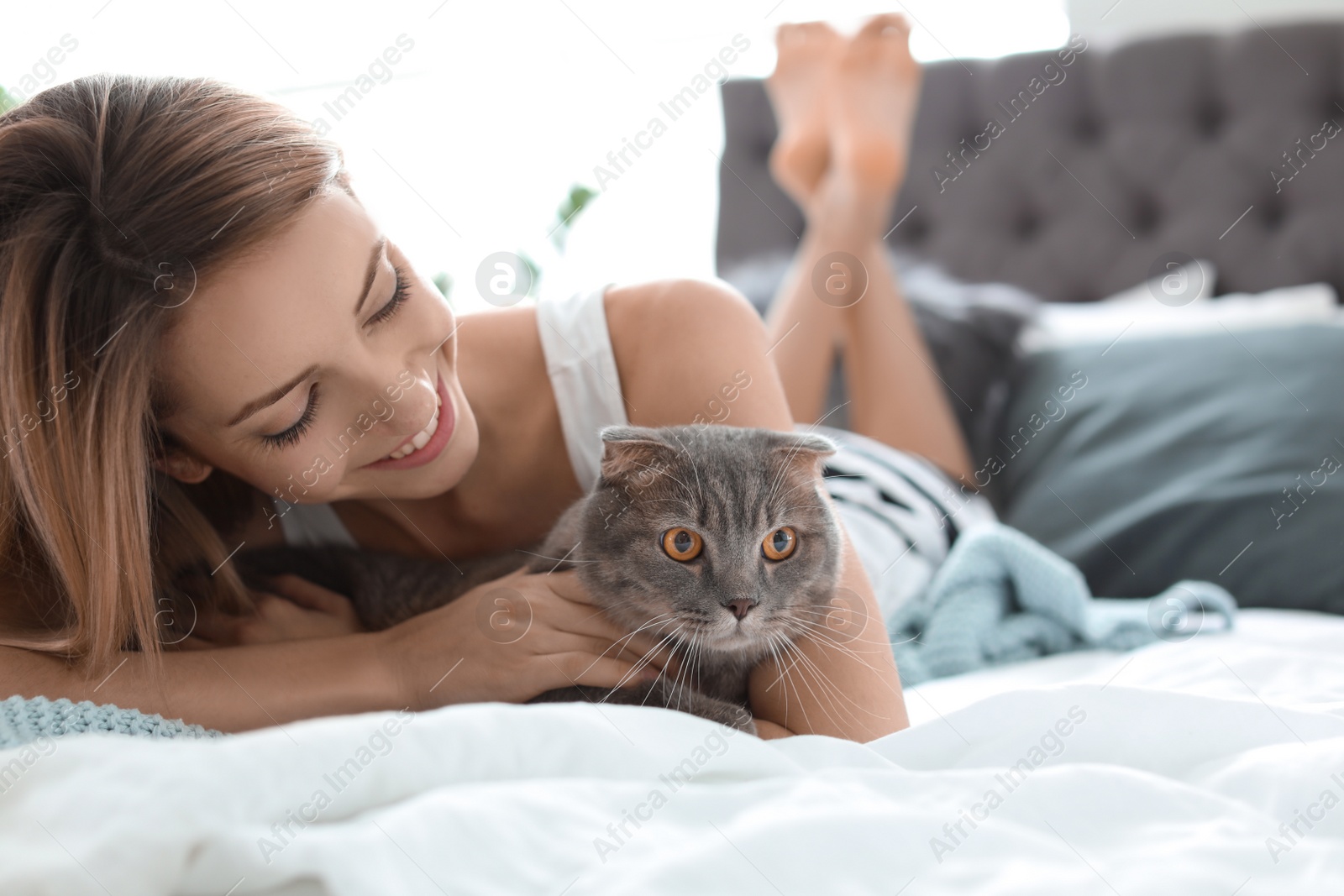 Photo of Young woman with her cute pet cat on bed at home