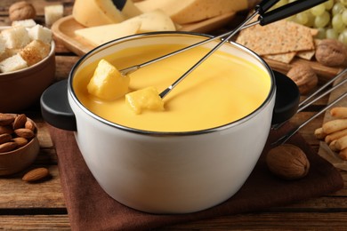 Photo of Pot of tasty cheese fondue and forks with bread pieces on wooden table