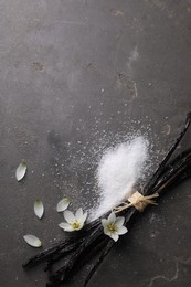 Photo of Vanilla pods, sugar, flowers and petals on gray textured table, flat lay. Space for text