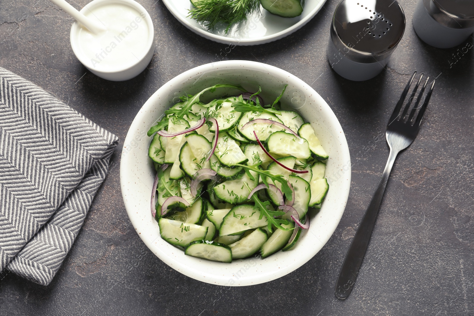 Photo of Delicious cucumber salad with onion and arugula in bowl served on grey table, top view