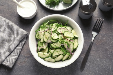 Photo of Delicious cucumber salad with onion and arugula in bowl served on grey table, top view