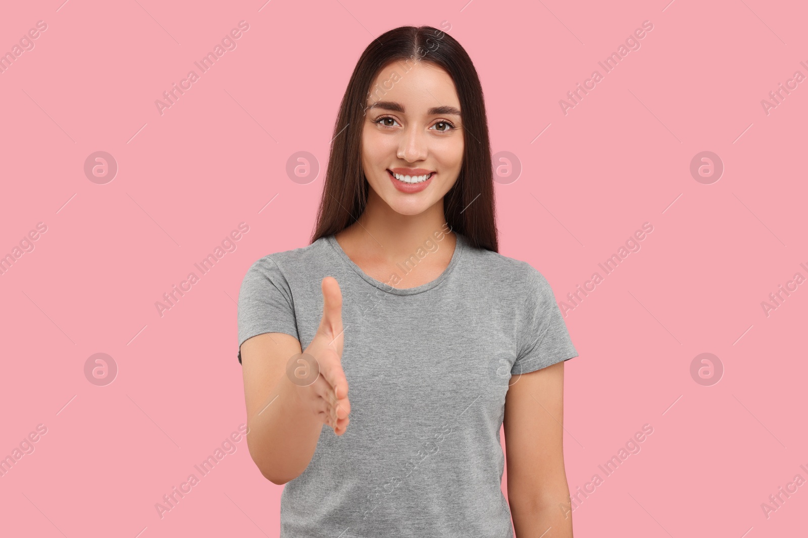 Photo of Happy young woman welcoming and offering handshake on pink background